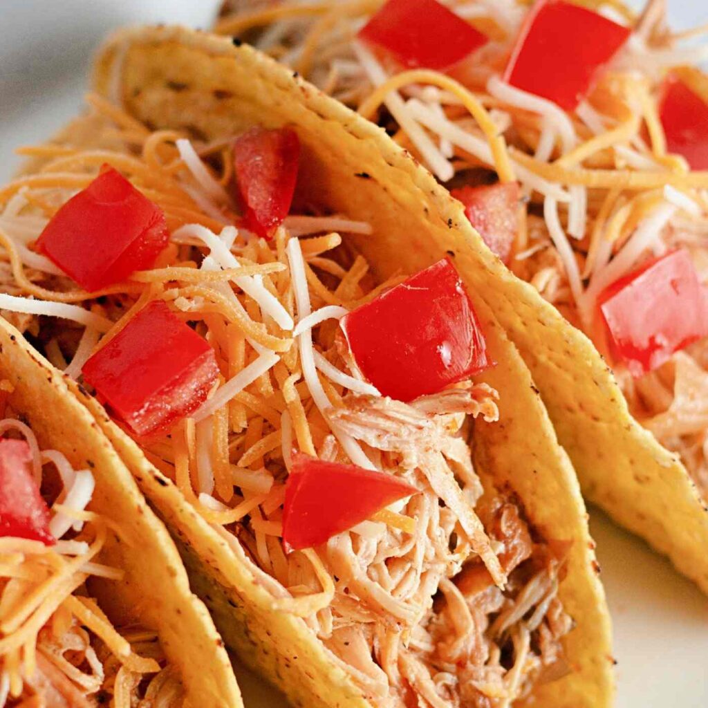 plate of crunch chicken tacos standing beside each other topped with tomatoes