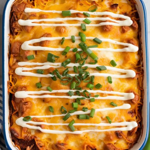 A rich and cheesy buffalo chicken casserole with a golden crust, topped with a drizzle of ranch and garnished with chopped green onions. Served in a white ceramic dish.