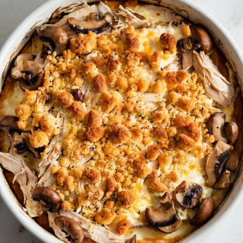 A white ceramic baking dish is filled with tender rotisserie chicken, sautéed mushrooms, and a rich, cheesy sauce.