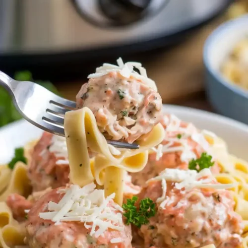 Juicy chicken meatballs coated in creamy Alfredo sauce, served over fettuccine, topped with shredded mozzarella and parsley. A cozy presentation with a fork twirling the pasta.