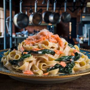 A richly detailed shot of a plate filled with creamy fettuccine tangled with spinach and salmon flakes, topped with a sprinkle of parmesan. set against a background of an industrial-style kitchen with hanging pots.
