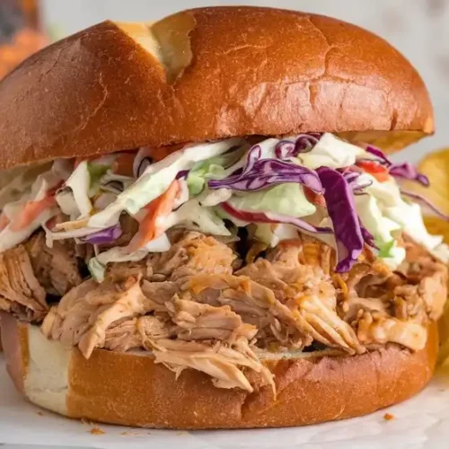 Shredded slow cooker BBQ chicken topped with cole slaw on a bun.