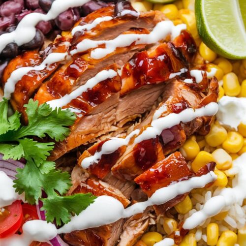A vibrant rice bowl filled with BBQ-glazed chicken, black beans, corn, cherry tomatoes, red onion, and fresh cilantro, drizzled with sour cream.