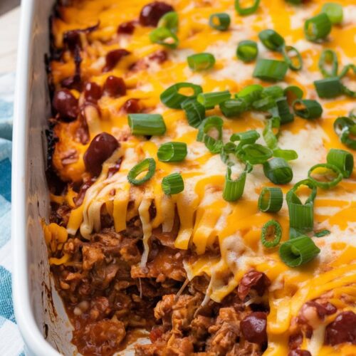 a baked casserole with melted cheddar and chili sauce, melted cheese on top, and garnished with chopped green onions