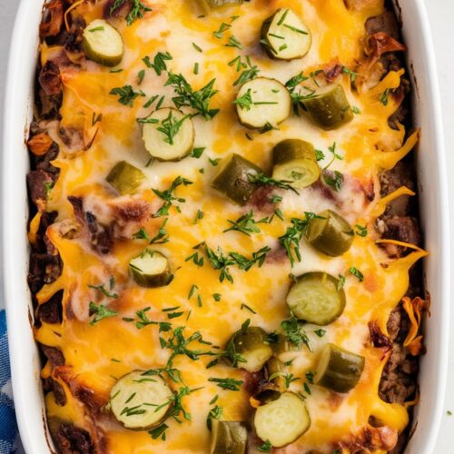 a baked casserole with melted cheddar with diced dill pickles, melted cheese on top, and garnished with chopped parsley