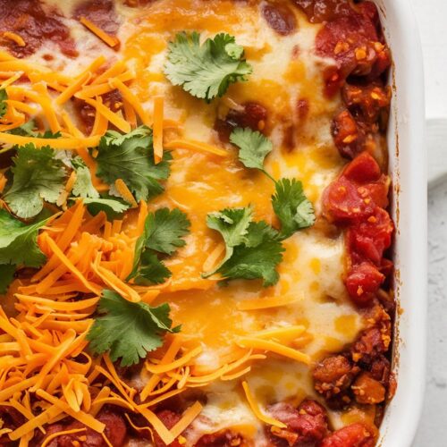 a baked casserole with a tomato-based sauce and melted cheese, melted cheese on top, and garnished with shredded cheddar and chopped cilantro