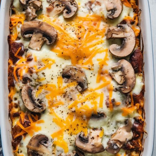a baked casserole with a creamy mushroom and cheese topping, melted cheese on top, and garnished with cracked pepper