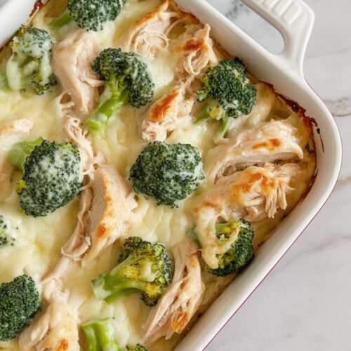 A bubbling Alfredo chicken bake in a white ceramic dish with broccoli and golden melted cheese.