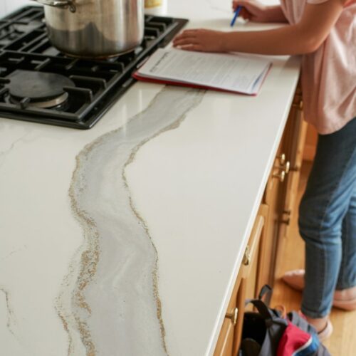 A busy kitchen scene with a multitasking home cook — one hand stirring a pot on the stove, t
