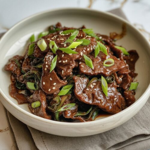 a bowl of beef steak sprinkled with sesame seeds and garnished with scallions