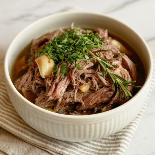 a bowl of delicious shredded and roasted chuck roaste with rosemary and garlic on top