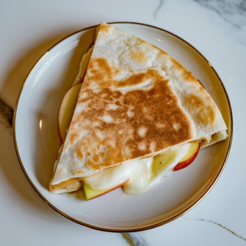 Close-up of a single apple and brie quesadilla wedge on a plate showing melted cheese and apple slices.