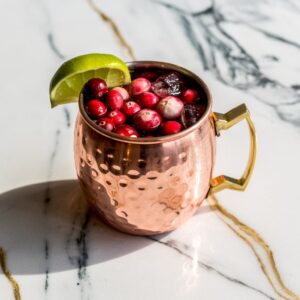 Cranberry Moscow mule served in a copper mug with lime wedge and fresh cranberries.