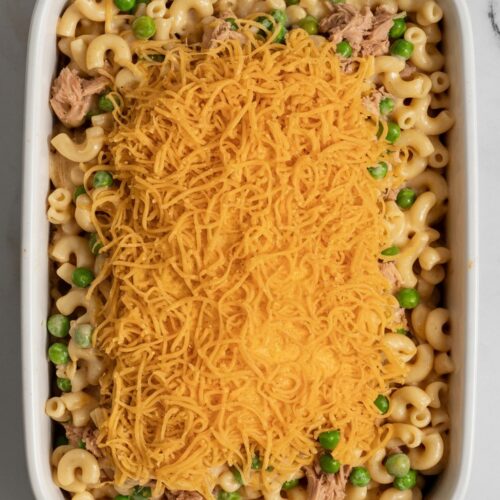 A white baking dish filled with dairy-free tuna noodle casserole, showing elbow macaroni coated in a creamy plant-based sauce with golden dairy-free cheese on top.