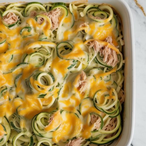 A keto-friendly tuna casserole made with spiralized zucchini and a creamy cheese sauce, baked in a white dish and viewed from above.