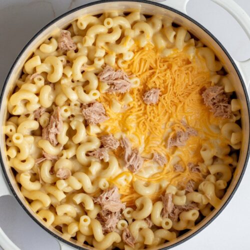 A white pot of creamy mac and cheese with tuna, made with elbow macaroni and shredded cheddar, viewed from the top.