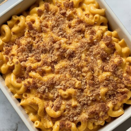 A white ceramic baking dish filled with creamy pumpkin mac and cheese topped with golden toasted breadcrumbs.