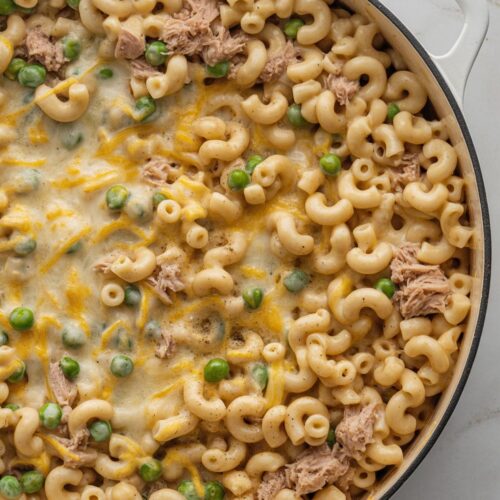 A large white skillet filled with creamy elbow macaroni, tuna, peas, and cheese, cooked entirely on the stovetop and shown from above.