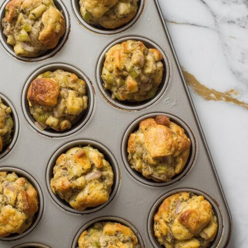 A muffin tin filled with stuffing and baked to golden perfection, celery and herbs can be seen peeking out