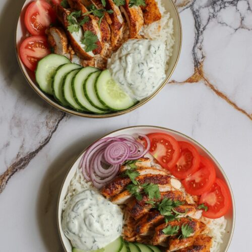 two chicken shawarma bowls with rice, cucumber, tomato, red onion, and a dollop of tzatziki, plated in shallow white bowls