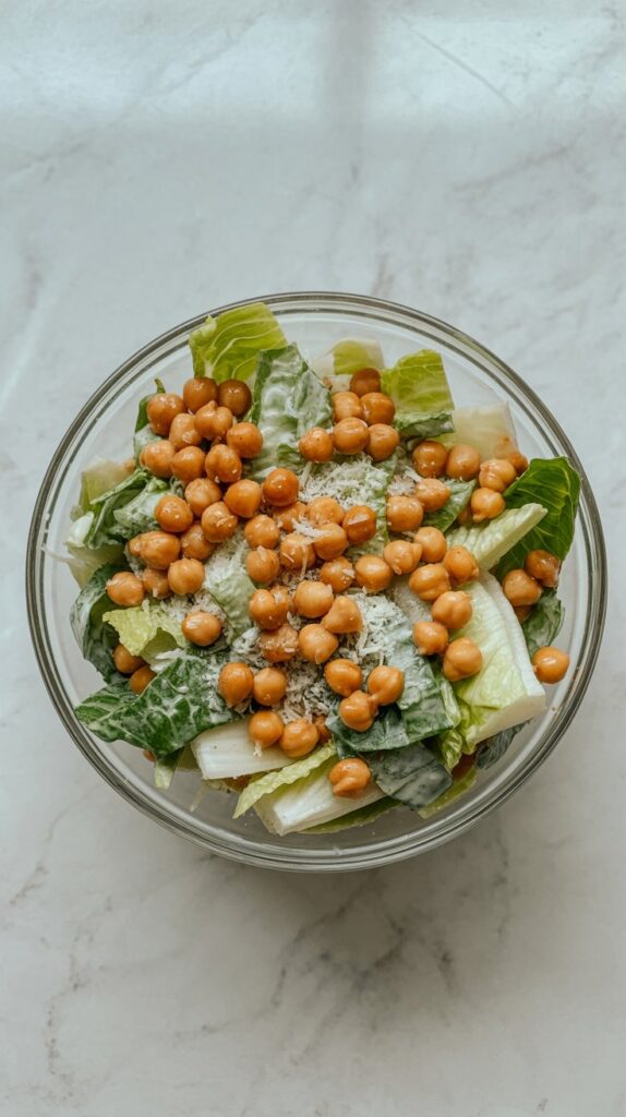 Overhead photo of Caesar salad in a glass bowl topped with crispy chickpeas and Parmesan.