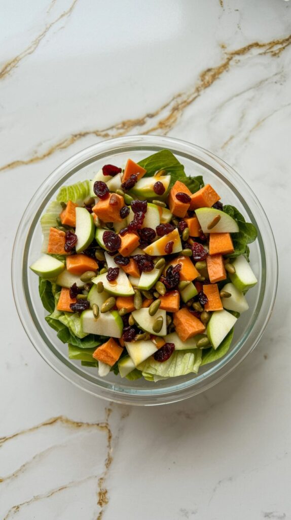 Overhead photo of chopped salad with apple, sweet potato, cranberries, and pepitas in a glass bowl.