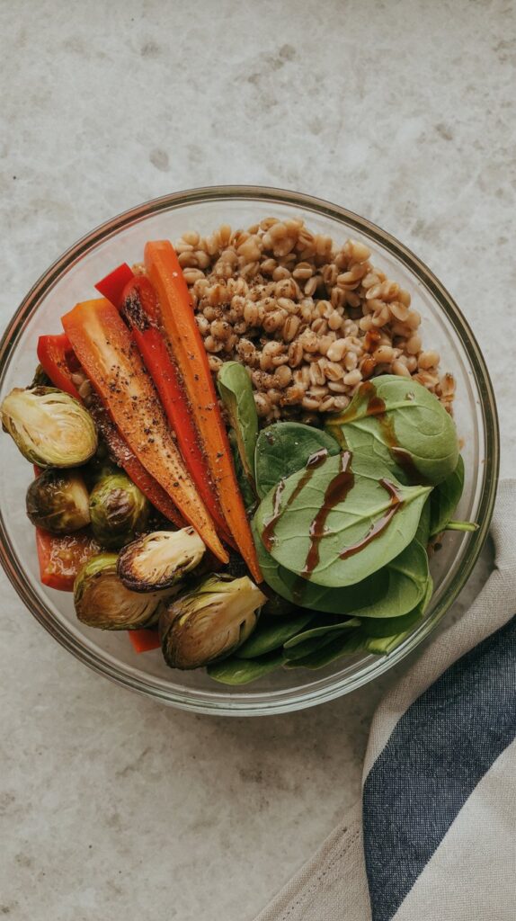 Overhead photo of grain bowl with roasted Brussels, carrots, and peppers over farro in a glass bowl.