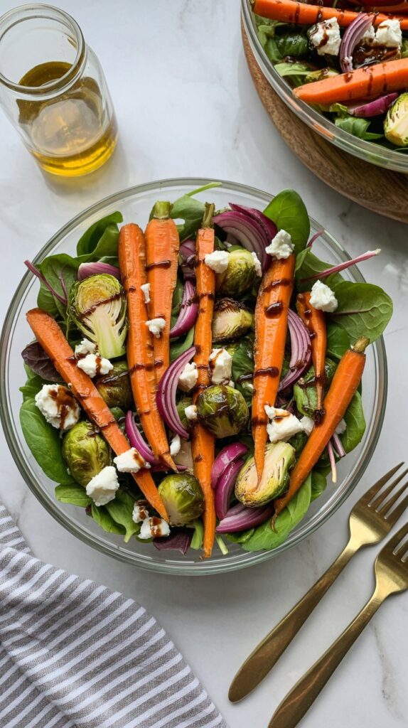 Overhead photo of roasted veggie salad with Brussels, carrots, onion, and goat cheese in a glass bowl.