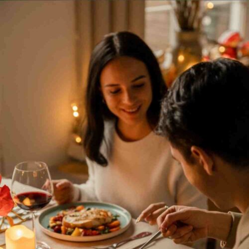 A young couple having a romantic dinner with lit candles and moody room with text "14 Romantic Dinners for Two. No Chef Hat Needed."
