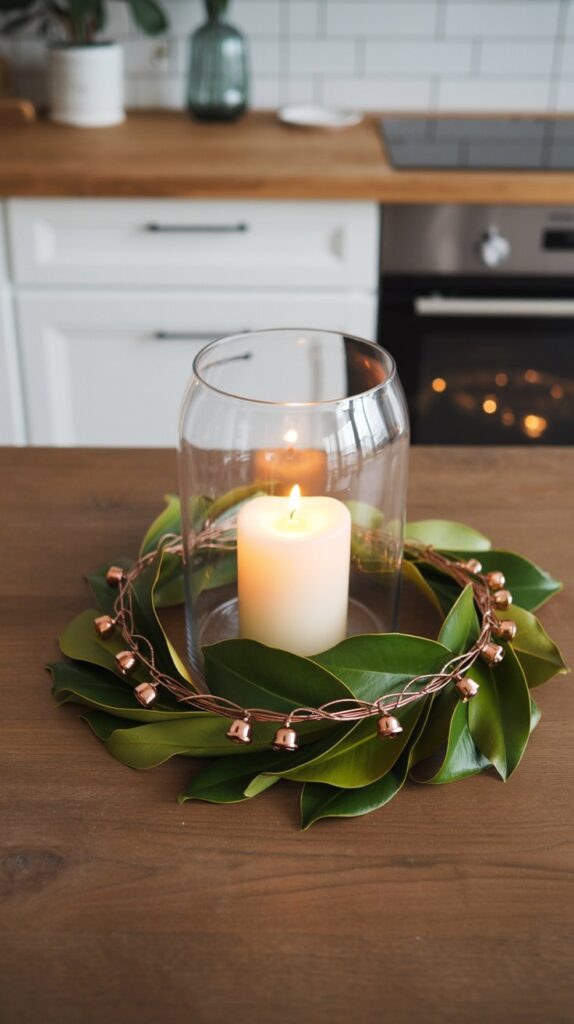 Flat magnolia wreath with woven copper wire and a glowing white pillar candle in a hurricane vase, styled as a minimalist kitchen table centerpiece.