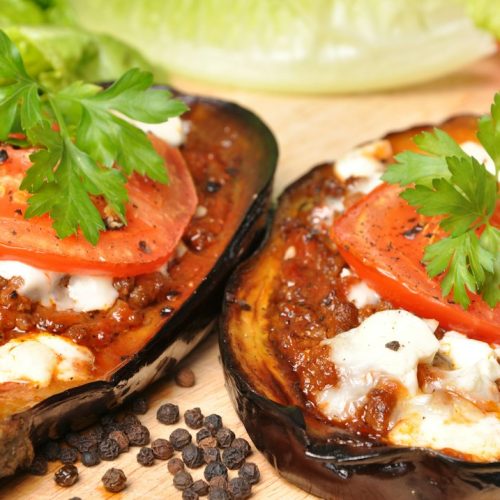 Baked vegetable boats stuffed with meat sauce, topped with melted cheese, tomato slices and parsley