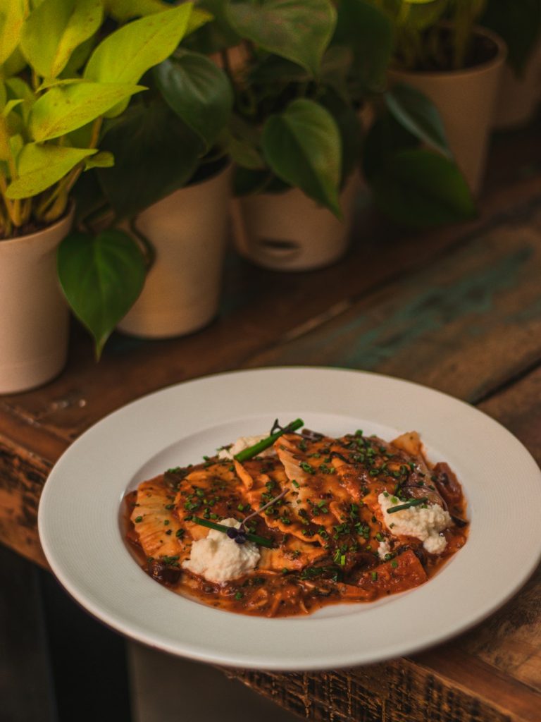 Beef enchiladas topped with red sauce, melted cheese and fresh herbs on a white plate
