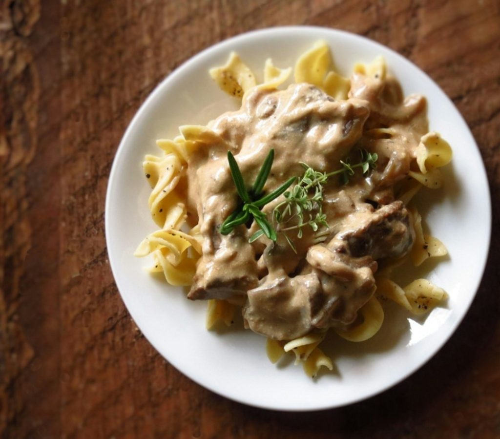 Beef stroganoff in creamy mushroom sauce over egg noodles on a white plate