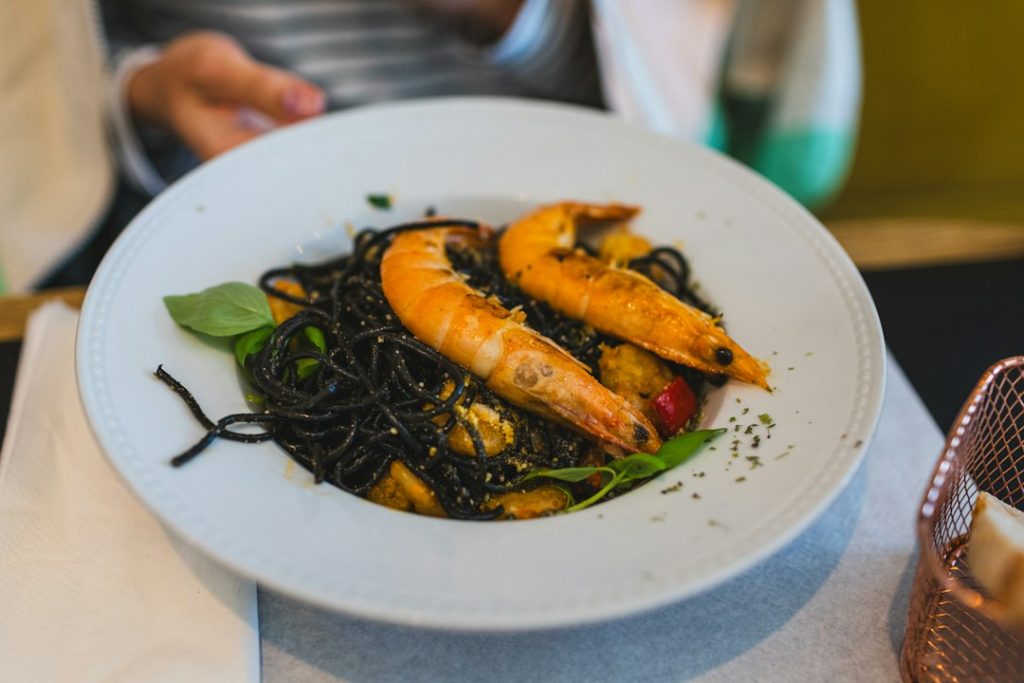 Black squid ink pasta with shrimp and fresh basil on a white plate
