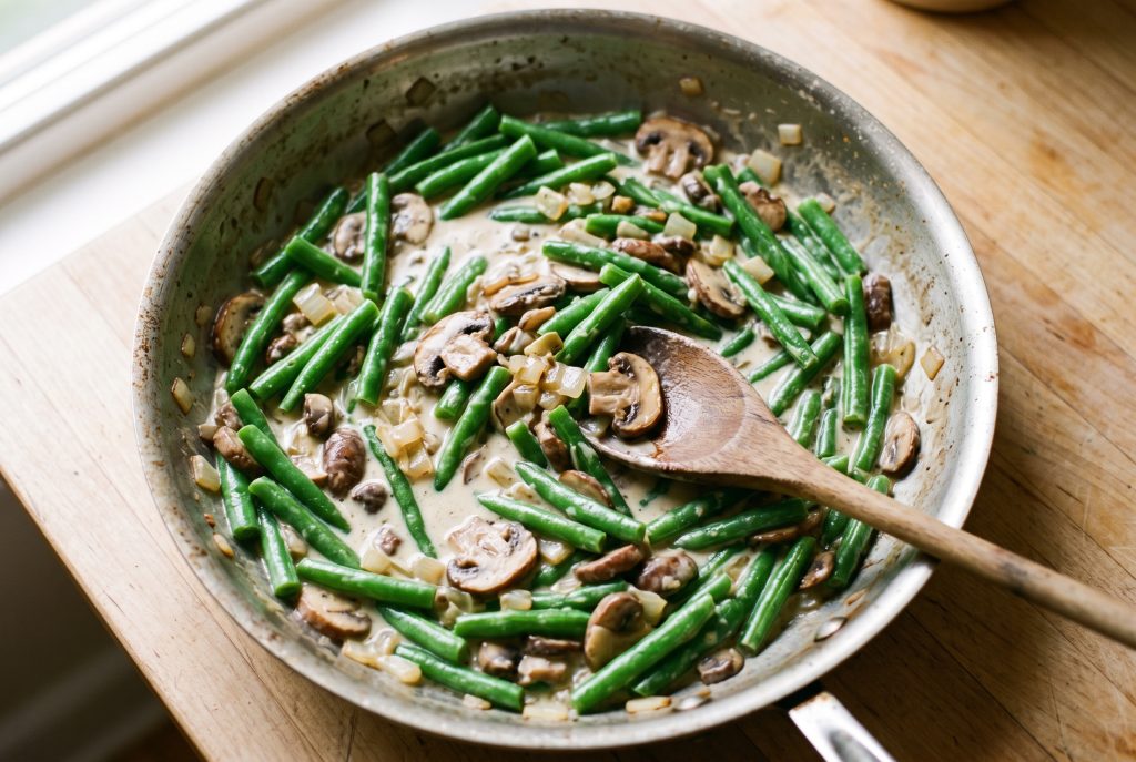 Blanched green beans stirred into homemade mushroom sauce in a skillet for green bean casserole
