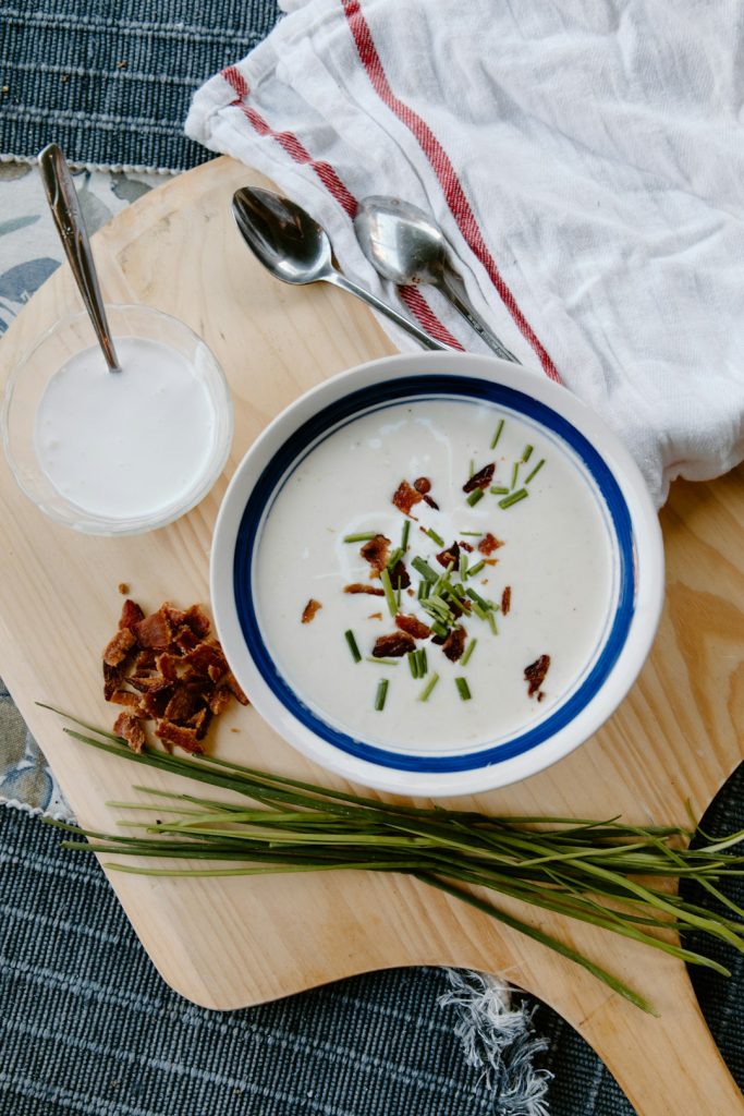 Bowl of creamy potato soup topped with chives and crispy bits, with fresh chives on a wooden board