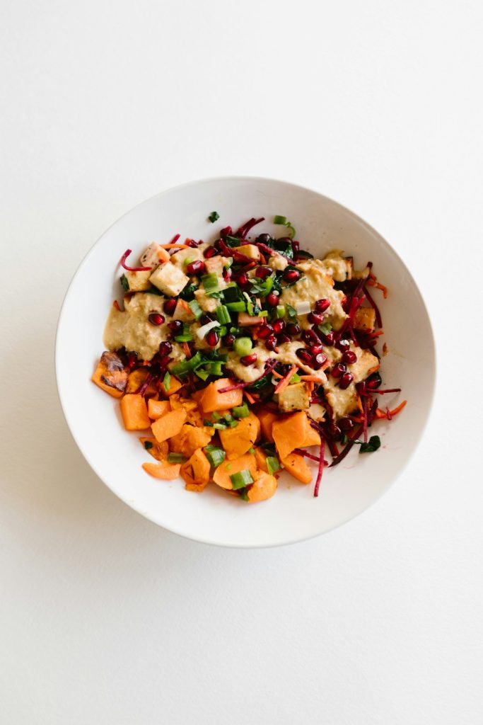 Bowl of roasted sweet potato salad with beets, pomegranate seeds and greens
