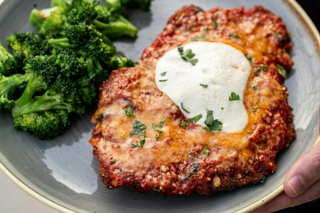 Breaded chicken parmesan with marinara and melted cheese next to steamed broccoli