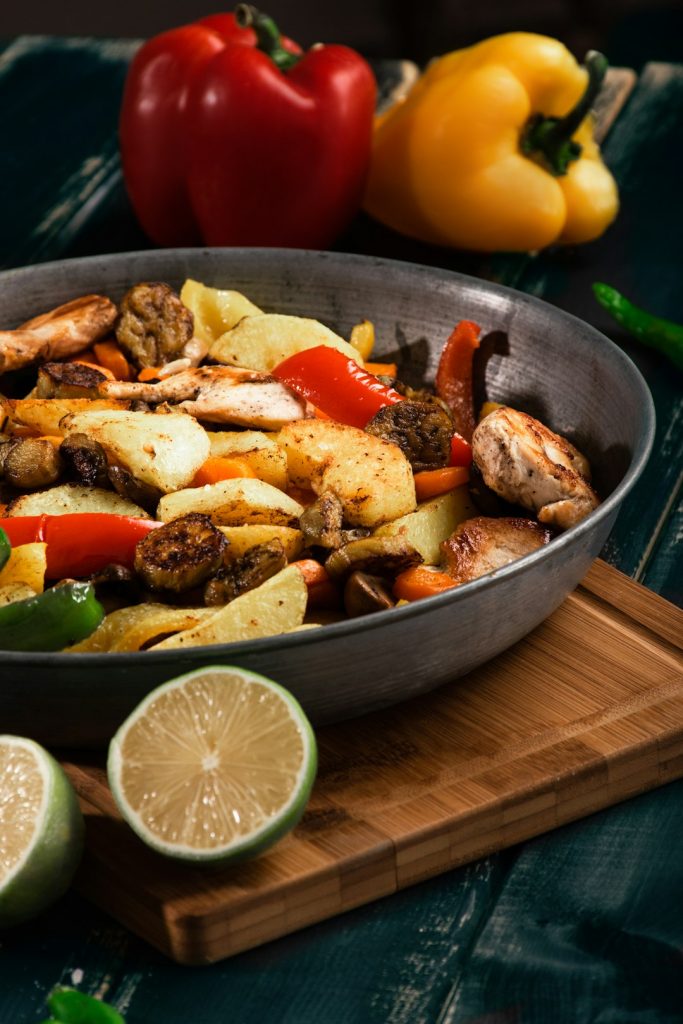 Chicken with sliced bell peppers and onions in a skillet with lime wedges