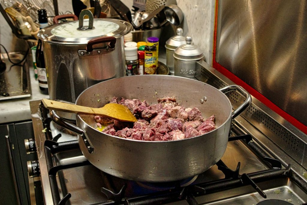 Chunks of meat browning in a pot on a gas stove before slow cooking