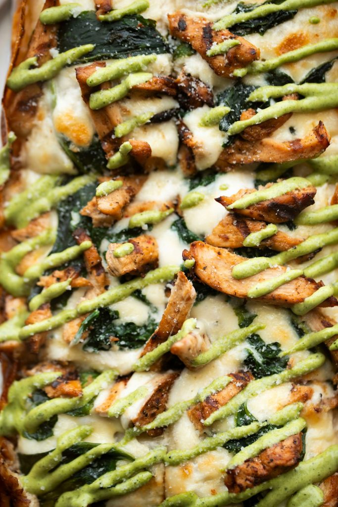 Close-up of baked chicken pieces with melted mozzarella, spinach and a drizzle of green pesto sauce