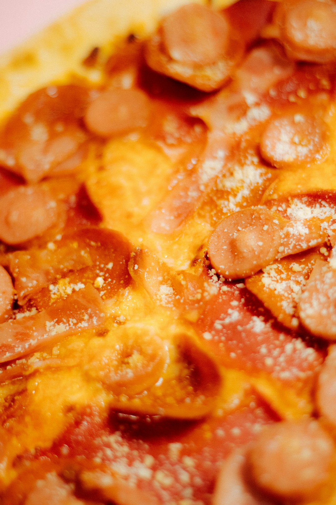 A close-up shot of a golden, crispy cheese base topped with sizzling pepperoni slices, crumbled bacon, and sausage in a black cast-iron skillet. The background features a rustic wooden kitchen counter with a pizza cutter and fresh herbs nearby. Large, bold text overlay in vibrant red and white reads: "Crustless Keto Pizza, Easy & Cheesy!"
