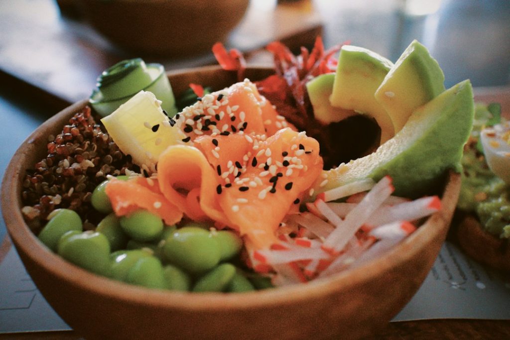 Fresh salmon bowl with avocado slices, edamame, radish and sesame seeds in a wooden bowl