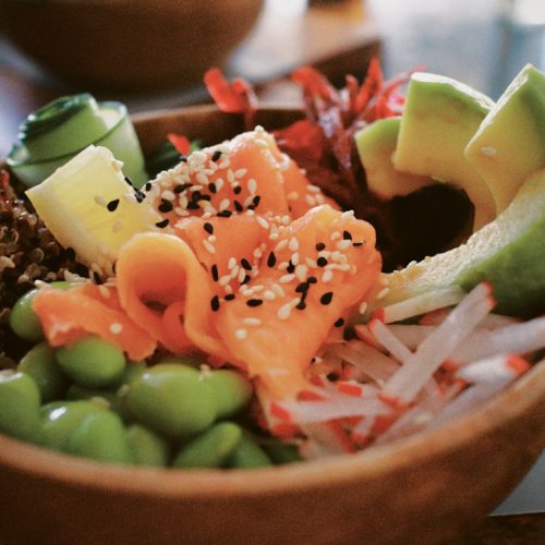 Fresh salmon bowl with avocado slices, edamame, radish and sesame seeds in a wooden bowl