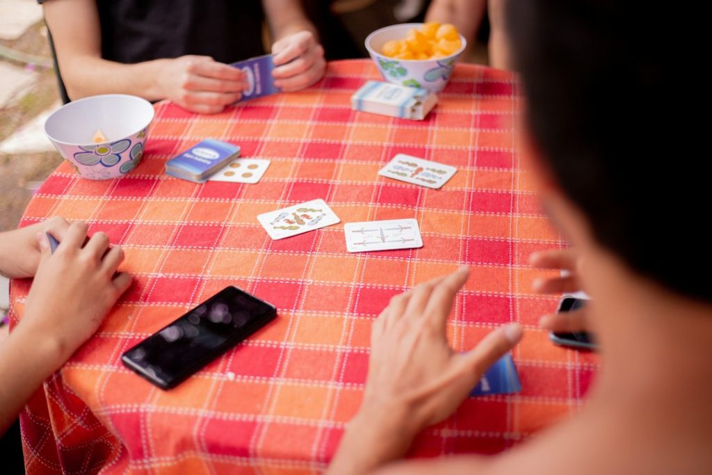Friends playing a card game on a checkered tablecloth with snacks nearby