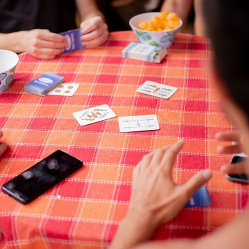 Friends playing a card game on a checkered tablecloth with snacks nearby