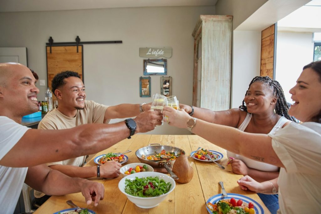 Friends raising their glasses in a toast around a wooden dinner table with shared dishes