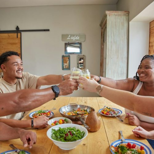 Friends raising their glasses in a toast around a wooden dinner table with shared dishes