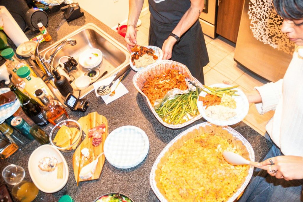 Friends serving themselves from shared potluck dishes on a kitchen counter