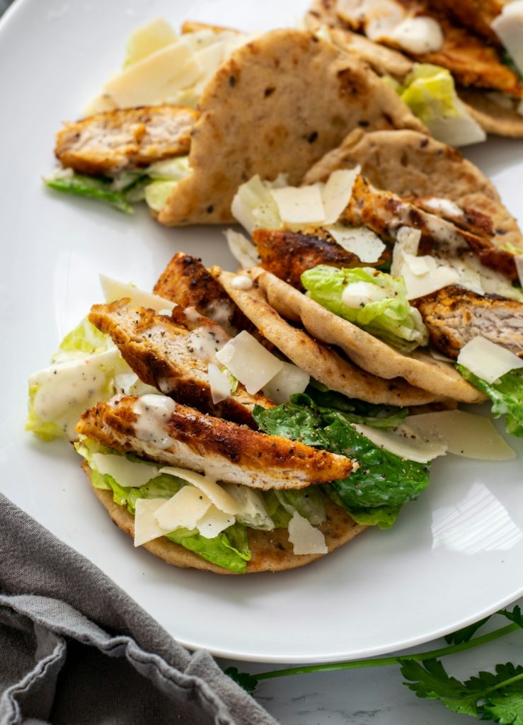 Grilled chicken tacos with lettuce and shaved cheese on a white plate